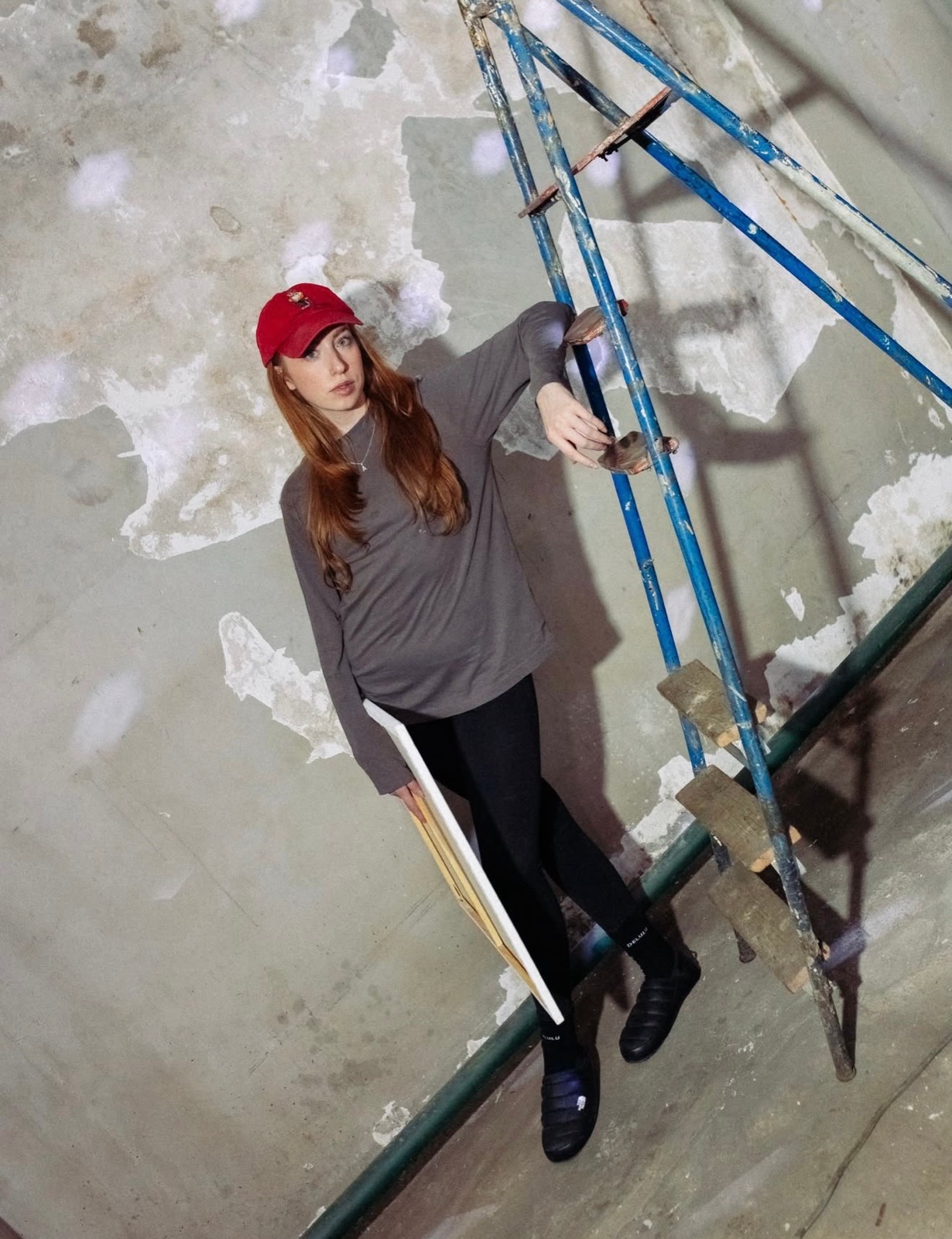 Anastasija Aleksejeva holding a canvas by a blue ladder in the industrial space