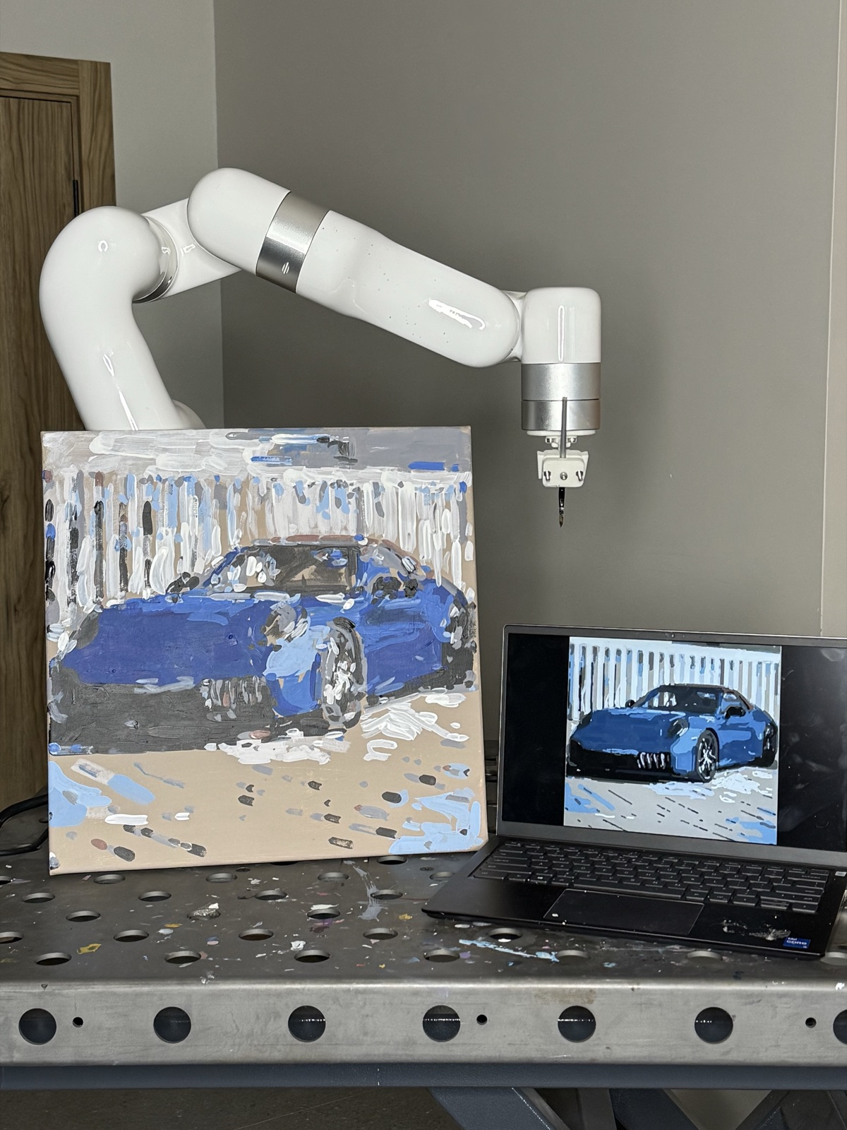 Robot-painted canvas of a blue Porsche next to the robotic arm and the digital reference on a laptop